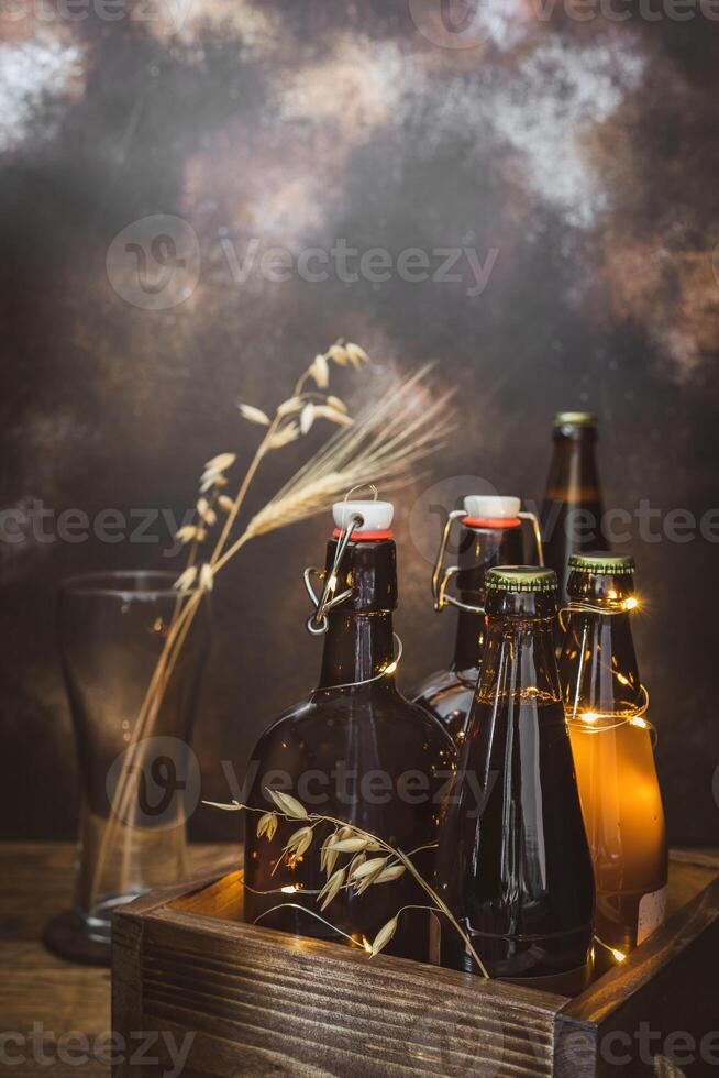 Bottles with cold, light and dark, unfiltered beer with ears of wheat in the empty glass on a broun background photo