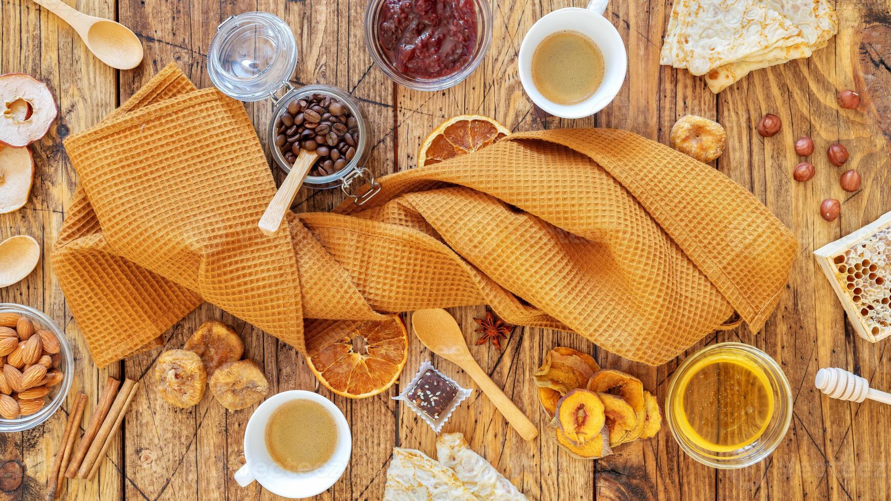 A folded kitchen towel around which pancakes, fruit chips, nuts, honey and two cups of coffee photo
