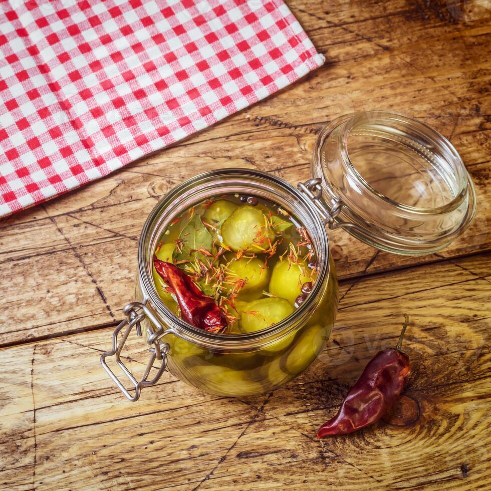 Homemade pickles in brine with spices in a glass jar on a wooden table with napkin photo