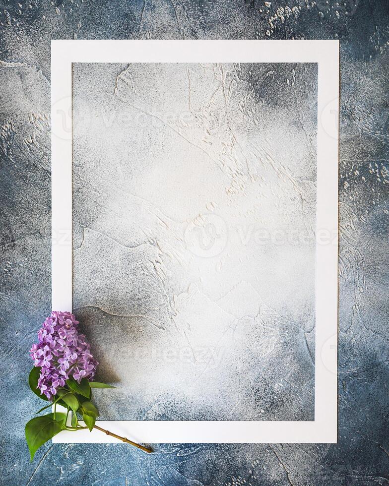 White frame and a fresh sprig of lilac on a blue textured background with copy space photo