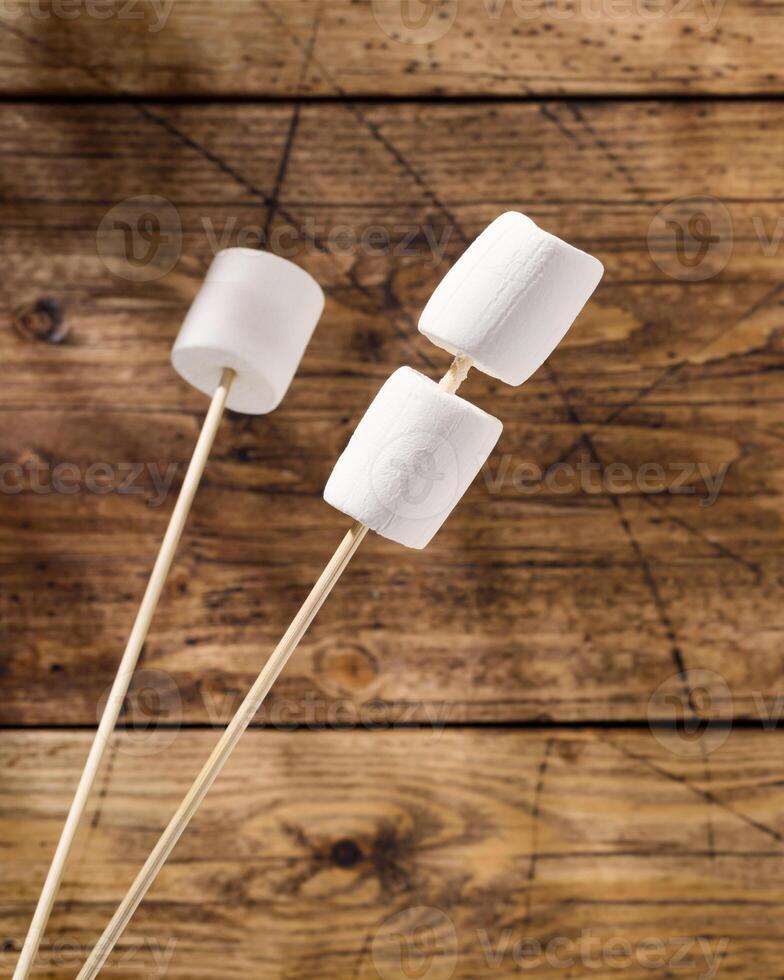 White marshmallow on wooden sticks and shade from palm leaves on a woodenbackground photo