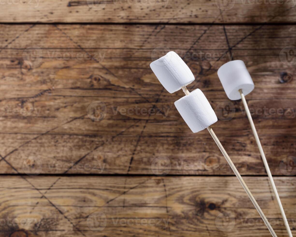 White marshmallow on wooden sticks and shade from palm leaves on a woodenbackground photo