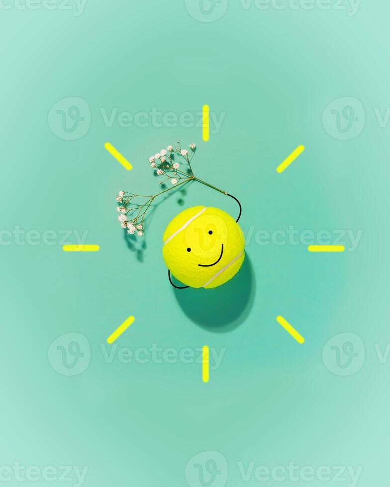 Large tennis ball in the form of a smiley face and flower on blue background photo