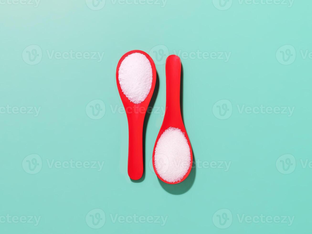 Red plastic spoons with sea salt and sugar on a blue background photo