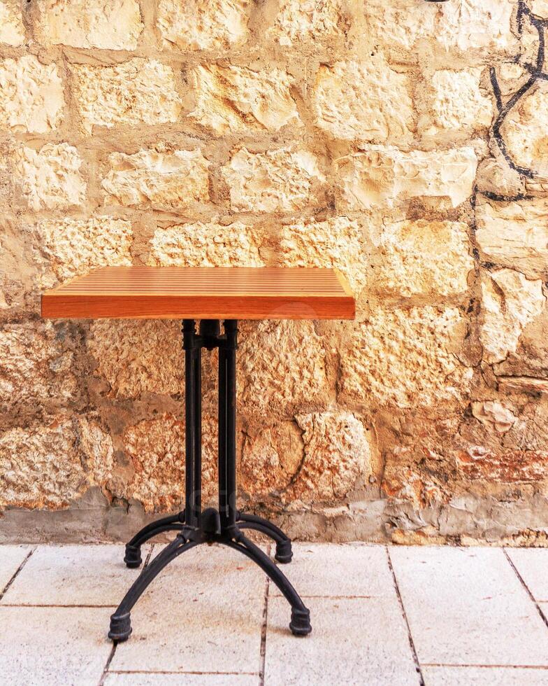 A wrought-iron table is not set against the background of a beautiful textured old wall made of large stone and decorated with wine bottles on a narrow street of the old European city photo