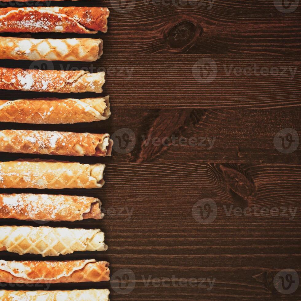 Waffle tubes with powdered sugar on a wooden background with copy space photo