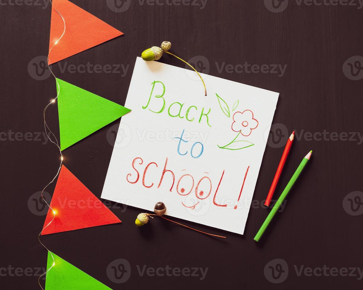 White sheet with inspiration back to school, pencils, paper flags and a light garland on a black chalkboard photo