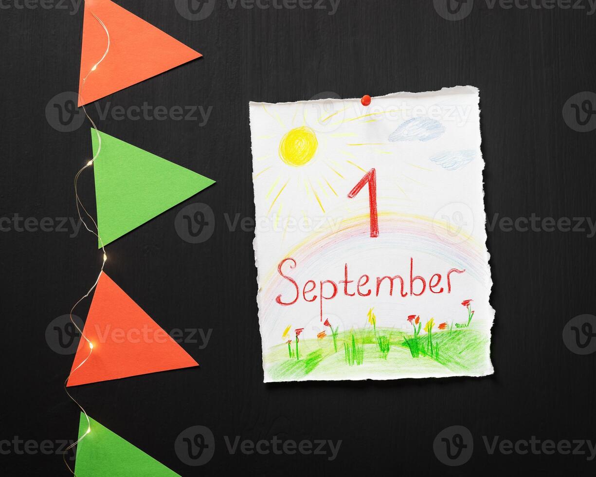 White sheet with a child's drawing and inspiration first september, paper flags and a light garland on a chalkboard photo
