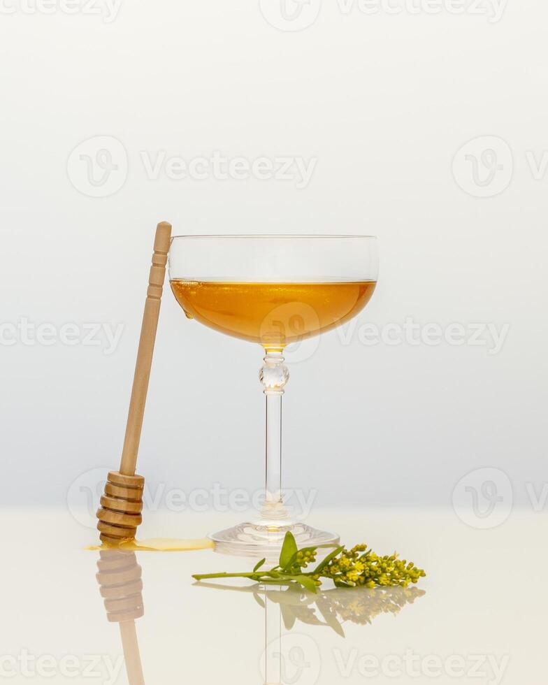Organic liquid honey in glass glass, yellow flower and honey dipper on a white table photo
