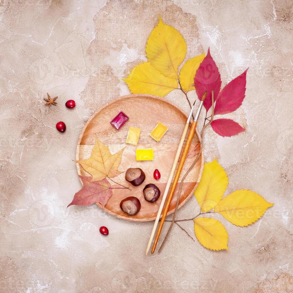 A wooden tray with dry leaves, watercolors, brushes, cranberries and chestnuts photo