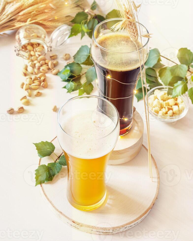 Two glasses of cold, light and dark, unfiltered beer, pistachios, ears of wheat and green leaves on a white background photo