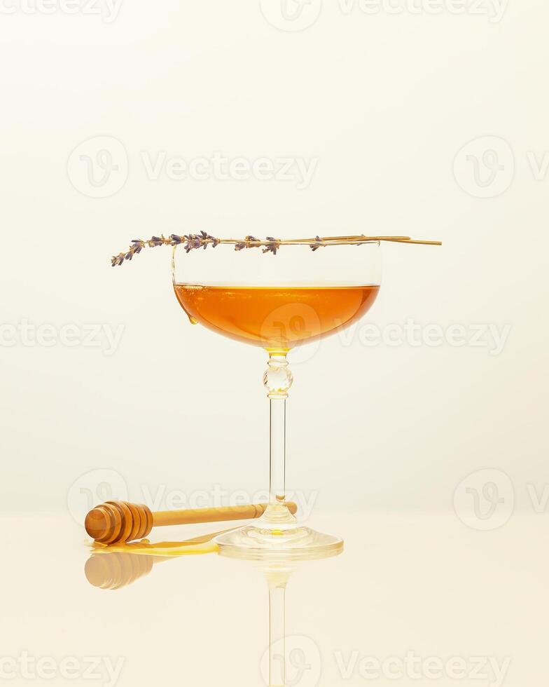 Liquid honey in glass glass, lavender sprigs and honey dipper on a white background photo