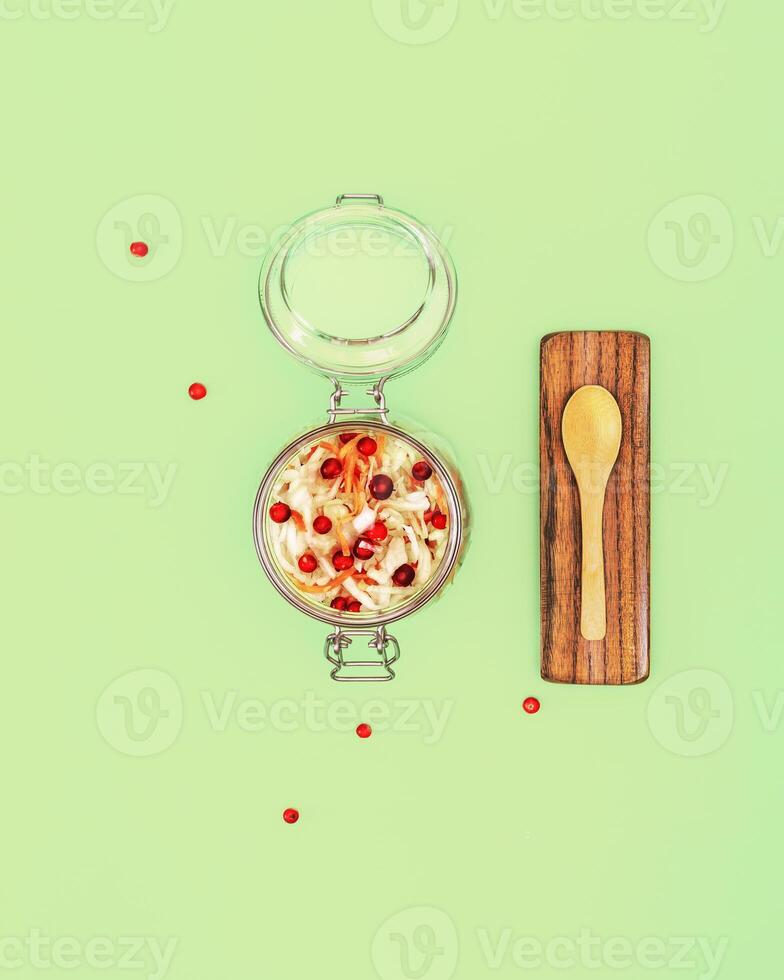 Fermented cabbage with cranberries and spices in a glass jar, wooden spoon on a white background photo