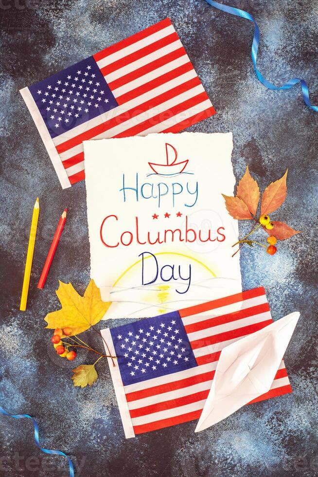 Withe sheet with kid drawing and inscription Happy Columbus Day, american flags, paper boat and autumn leaves photo