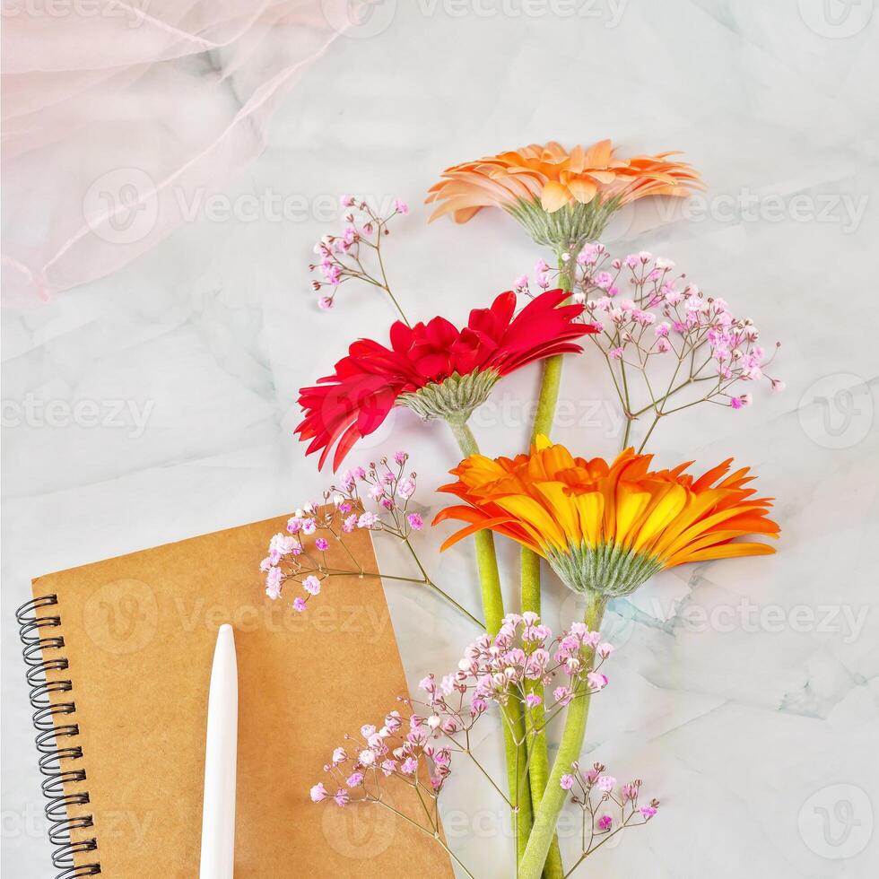 A bouquet of colorful gerberas with a notebook, a pen and a light chiffon scarf photo