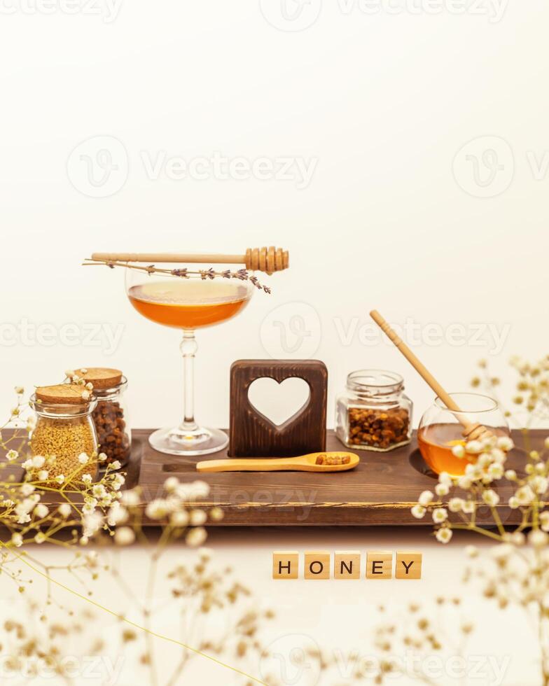 Bee products and honey in glass jars with honey dipper and wooden inscription honey on a white table photo