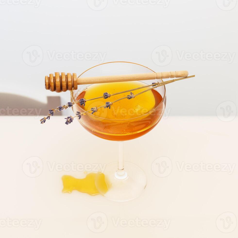 Gold liquid honey in glass glass, lavender sprigs and honey dipper on a white table photo