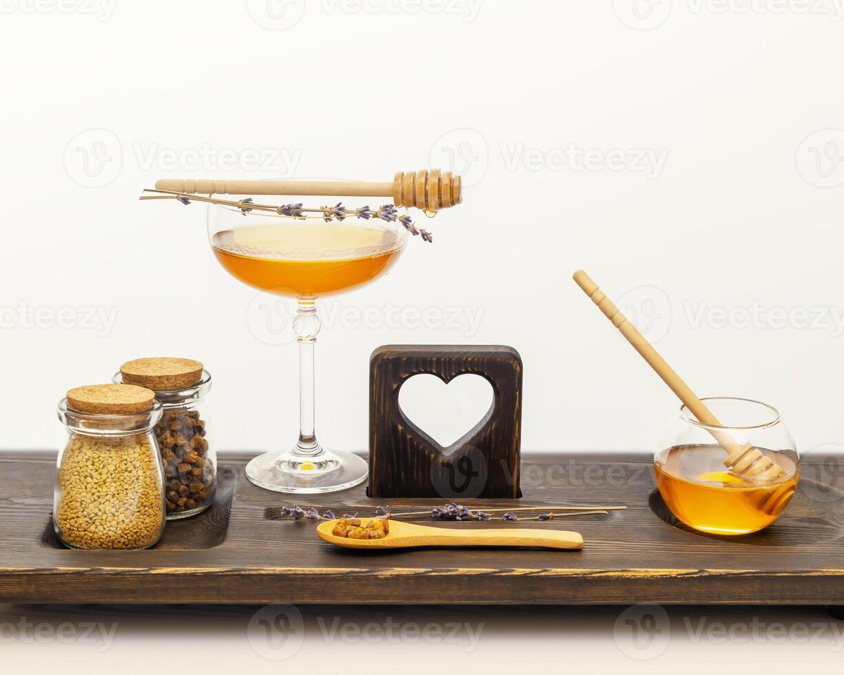 Bee products and honey in glass jars with honey dipper and lavender flowers on a wooden board photo