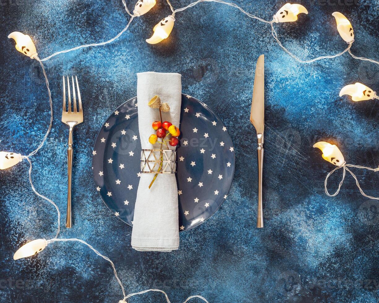 Helloween holiday composition with festive plate with a knife, fork and napkin on a blue background photo