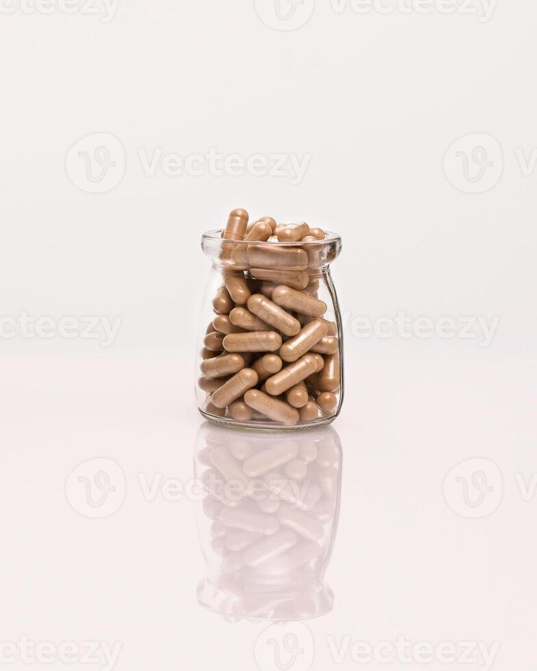 Organic herb capsules in a glass bottle on a white table with reflection photo