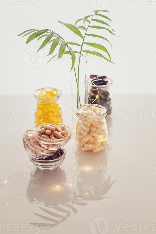 Different kind of vitamins in glass bottles, palm leaves and lighting garland on a light background photo