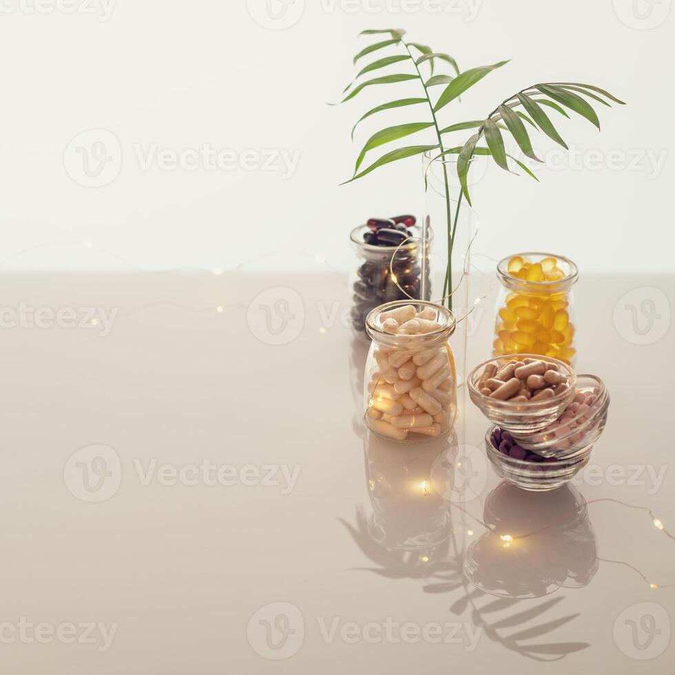 Different kind of vitamins in glass bottles, palm leave and lighting garland on white background photo