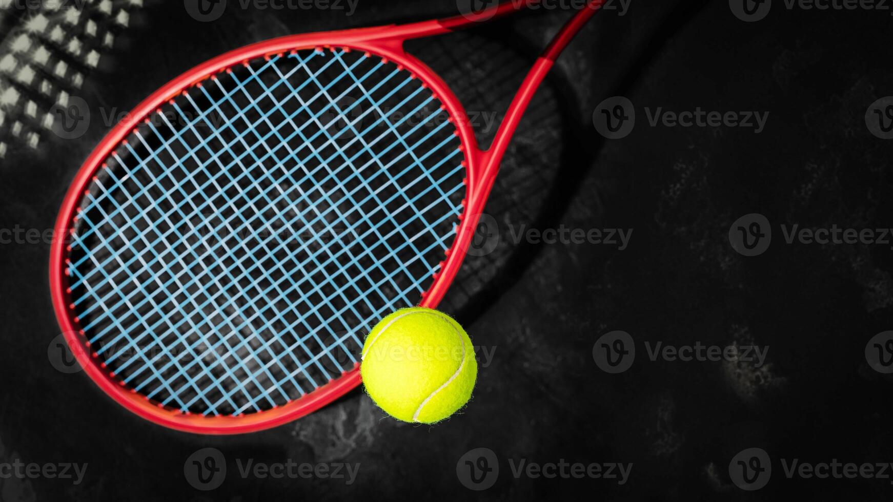 Yellow tennis ball with red racket on a black background with copy space photo
