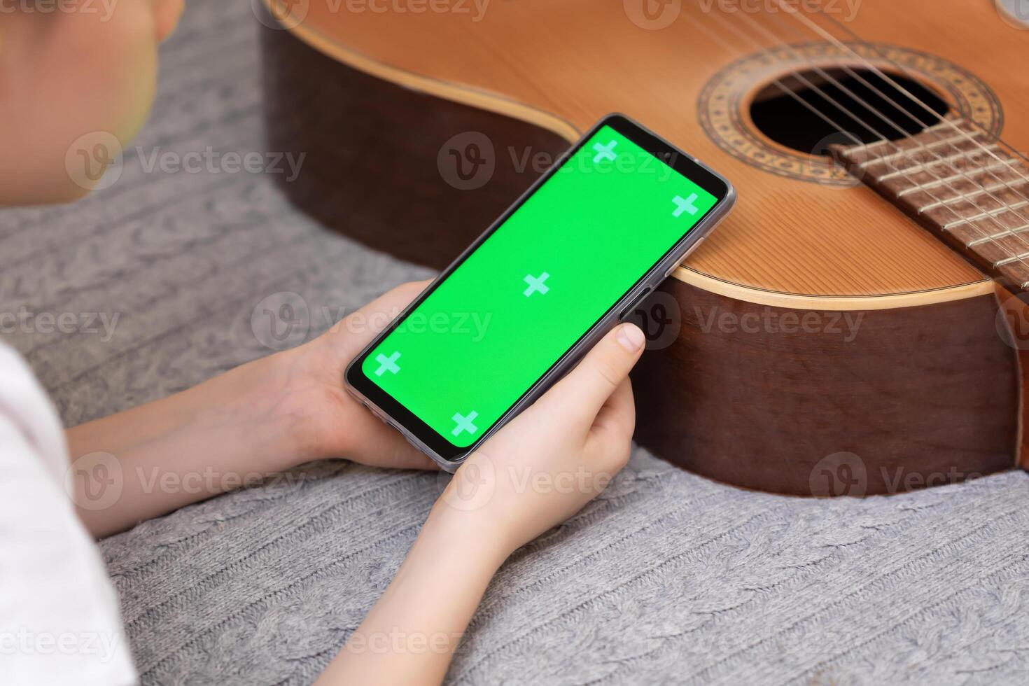 Boy with guitar holding the smartphone with green screen photo