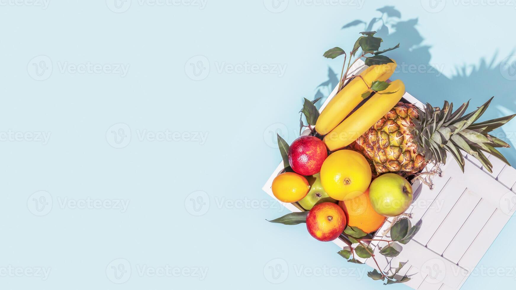 Natural tropical fruits with leaves in a wooden box on a blue background photo