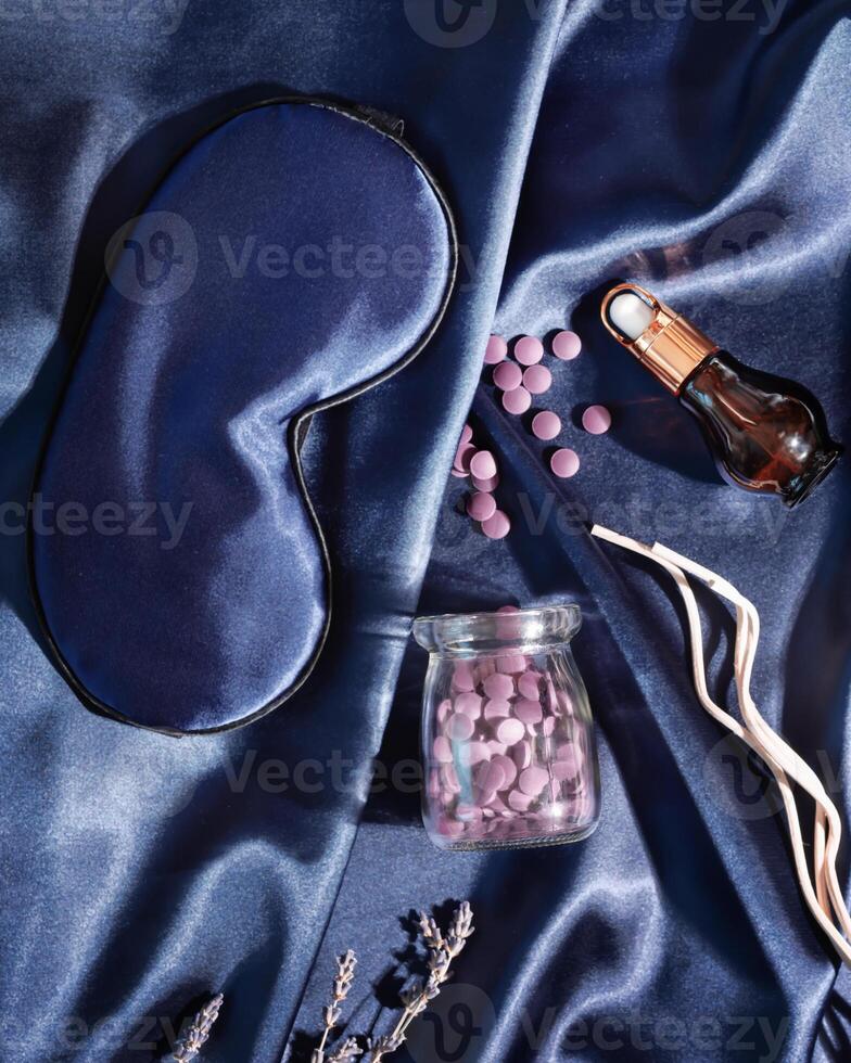 Mask for sleep, sleeping pills and herbal oil on a blue silk bed linen photo