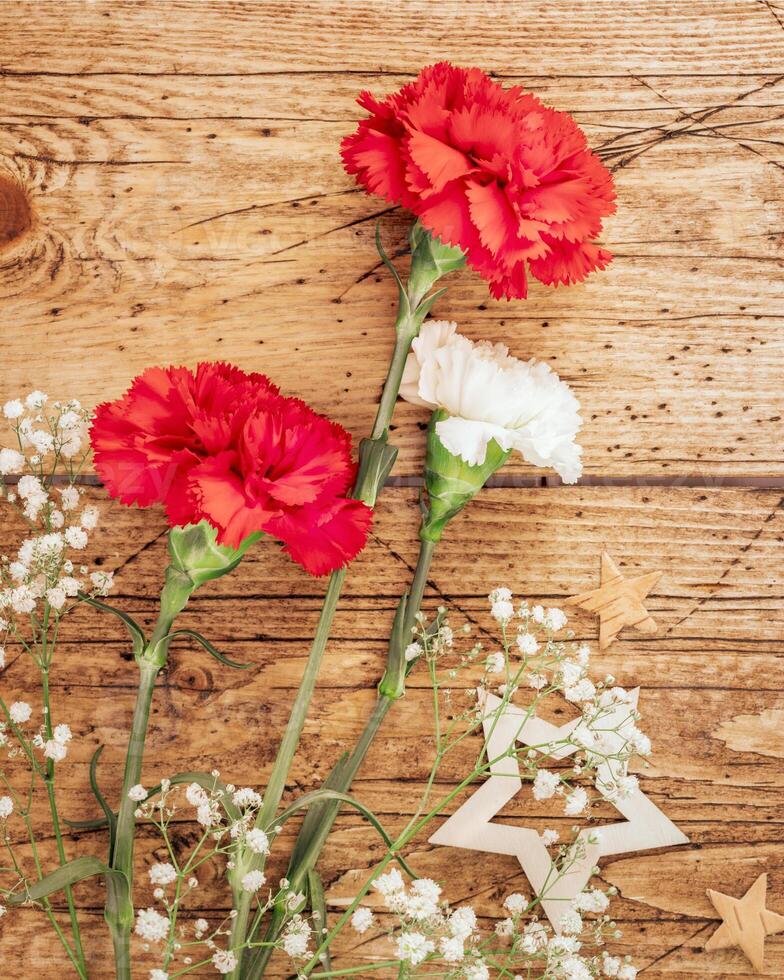 Red and white carnations and decorative stars on a wooden background photo