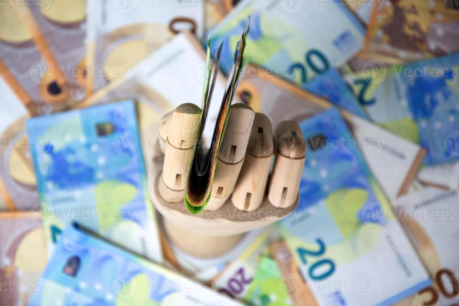 A wooden hand holds a stack of twenty Euro banknotes against a backdrop of additional twenty Euro notes photo