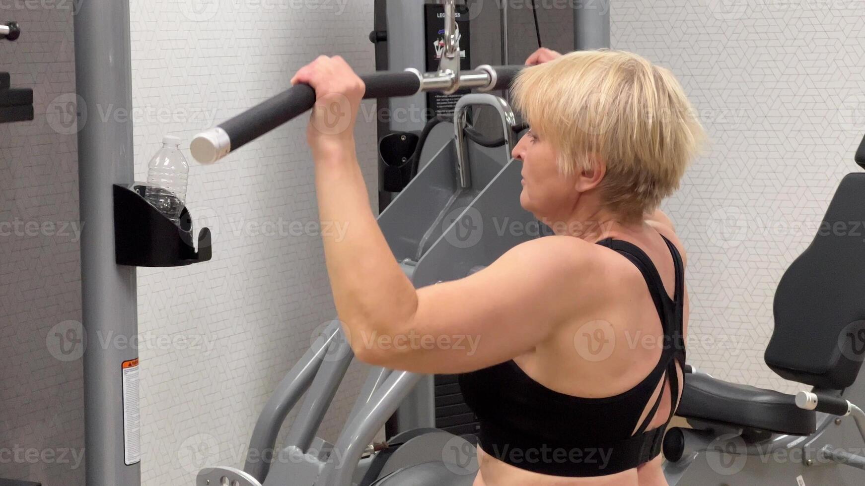 An individual is engaged in an intense workout session using a cable pulley machine at the gym against a geometrically patterned backdrop. photo