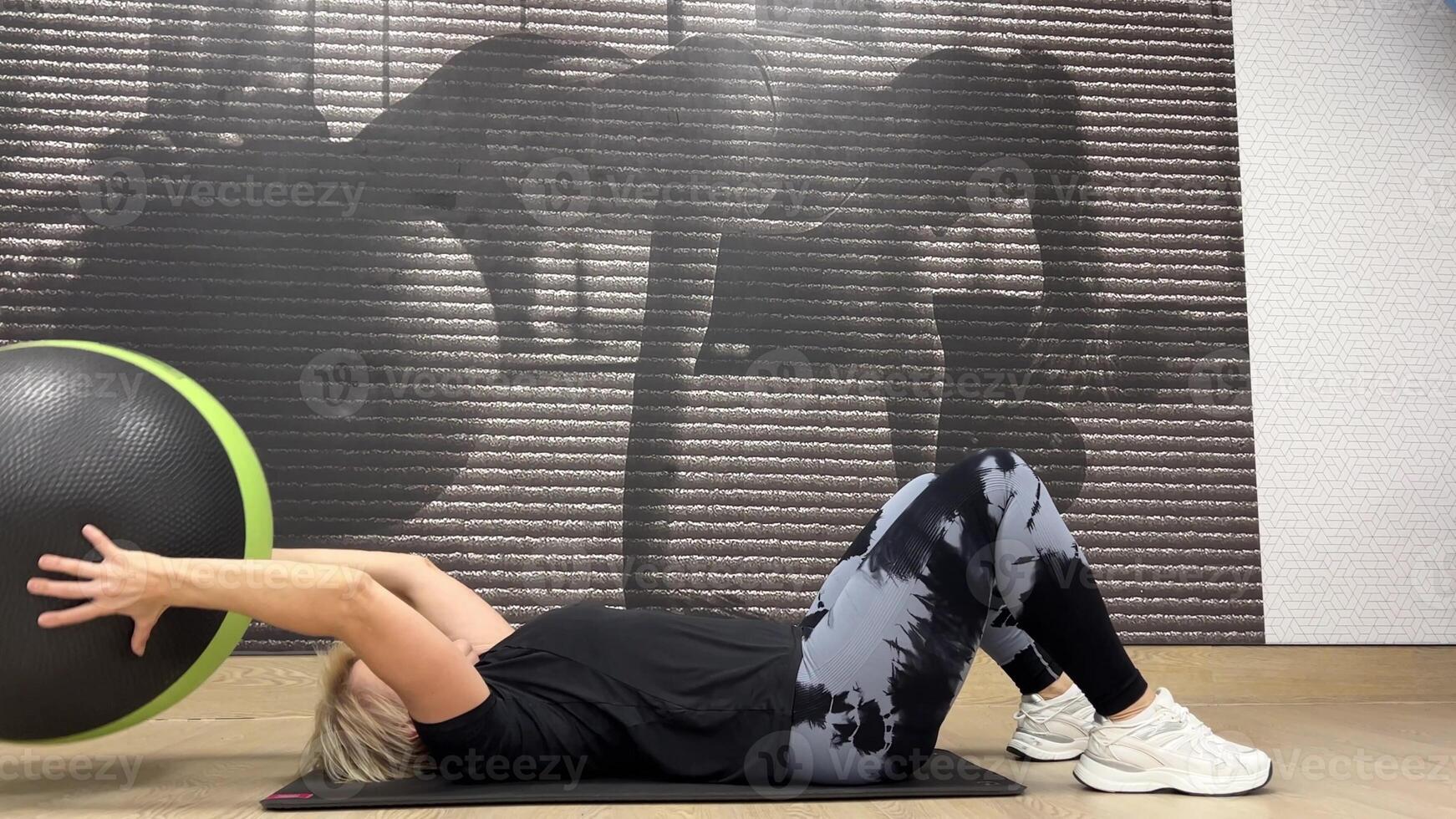 Person is engaged in fitness exercise with large, green-trimmed black exercise ball. photo