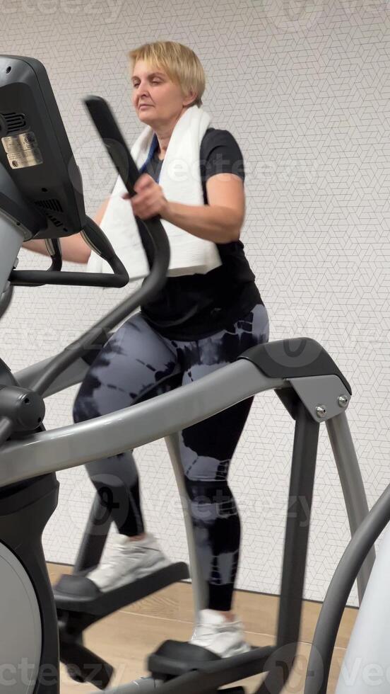 A fat blonde 55-60 years old walks actively to burn fat. A woman is training in the gym. photo