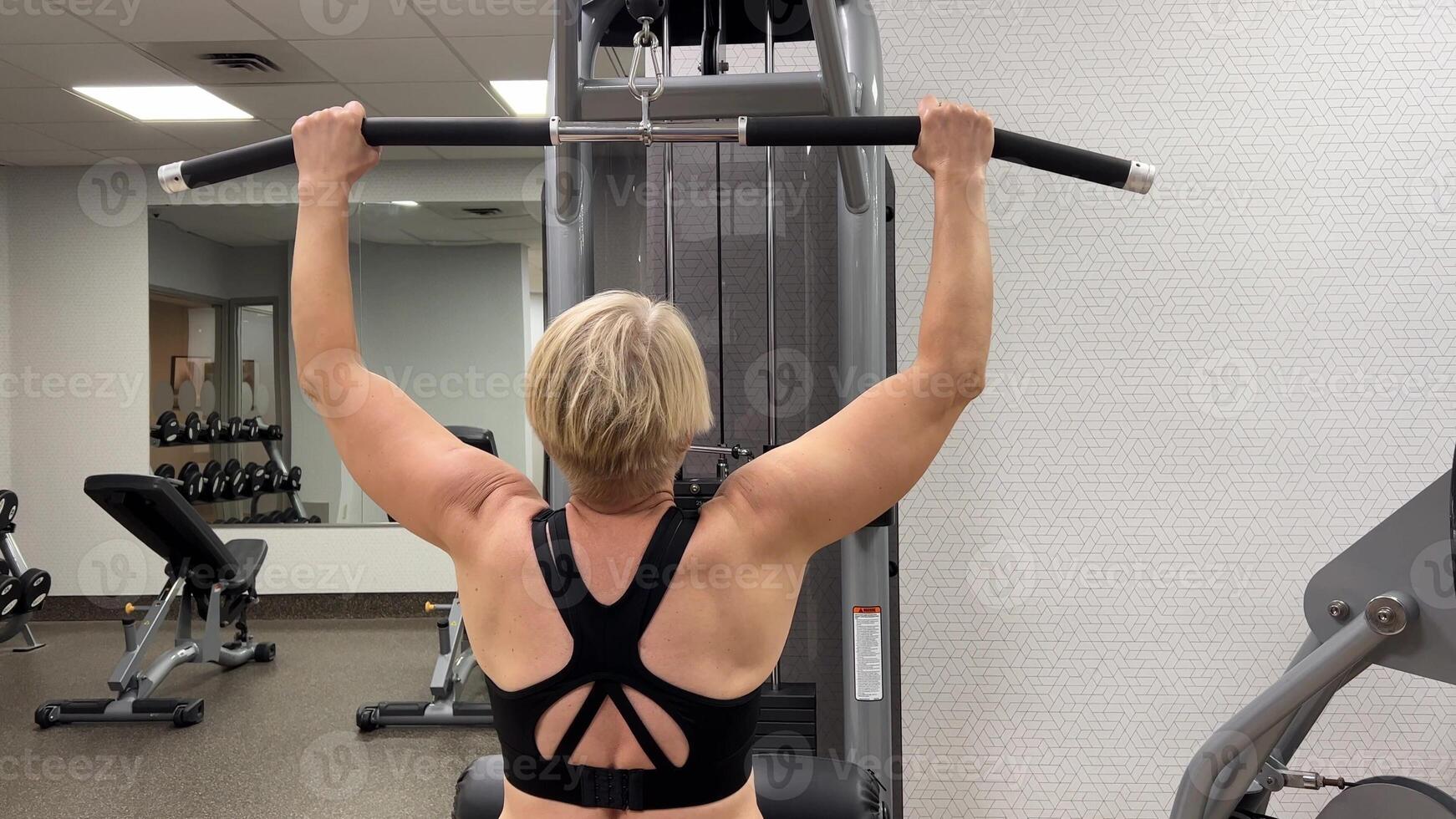 An adult Caucasian woman trains pull-ups with a horizontal bar on a machine in the gym. Rear view, horizontal . photo