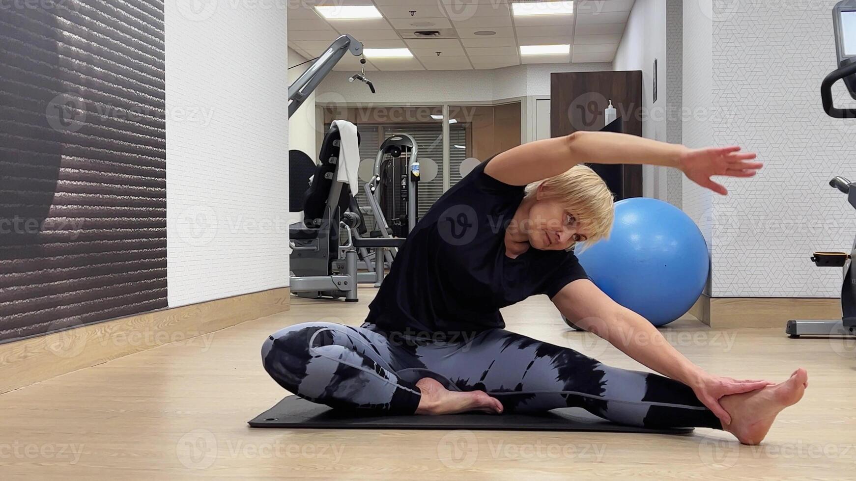 Senior woman doing stretching exercises on yoga mat. A plump European woman bends over to stretch the muscles of her arms and legs. photo