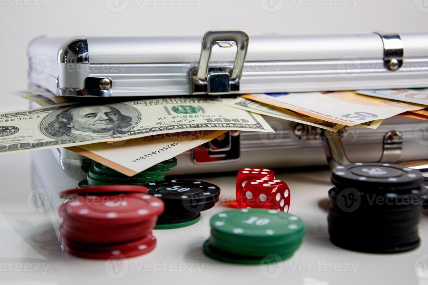 A silver case with cash peeking out sits on a white surface next to stacks of poker chips and dice photo