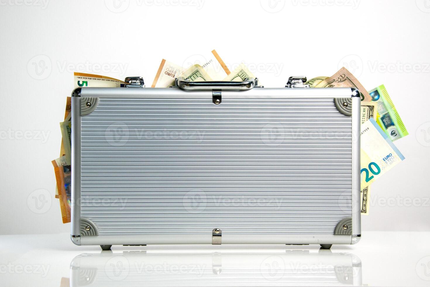 A silver aluminum briefcase with a slightly open latch and a few protruding bills of various currencies photo