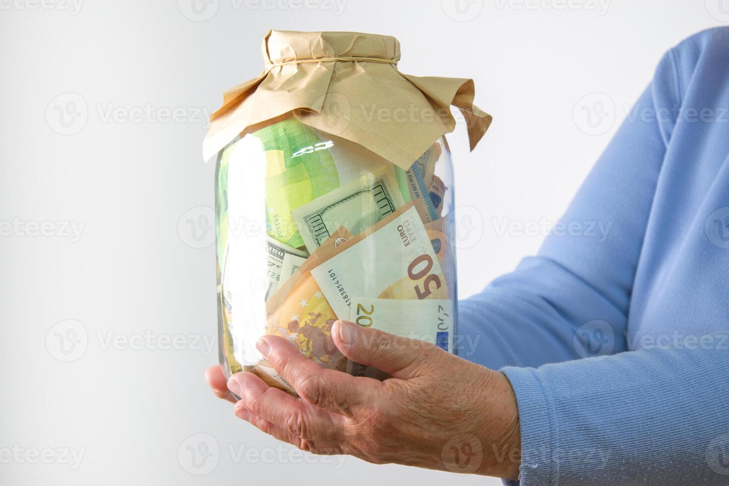 A persons hands are holding a glass jar filled with US dollar and euro bills photo