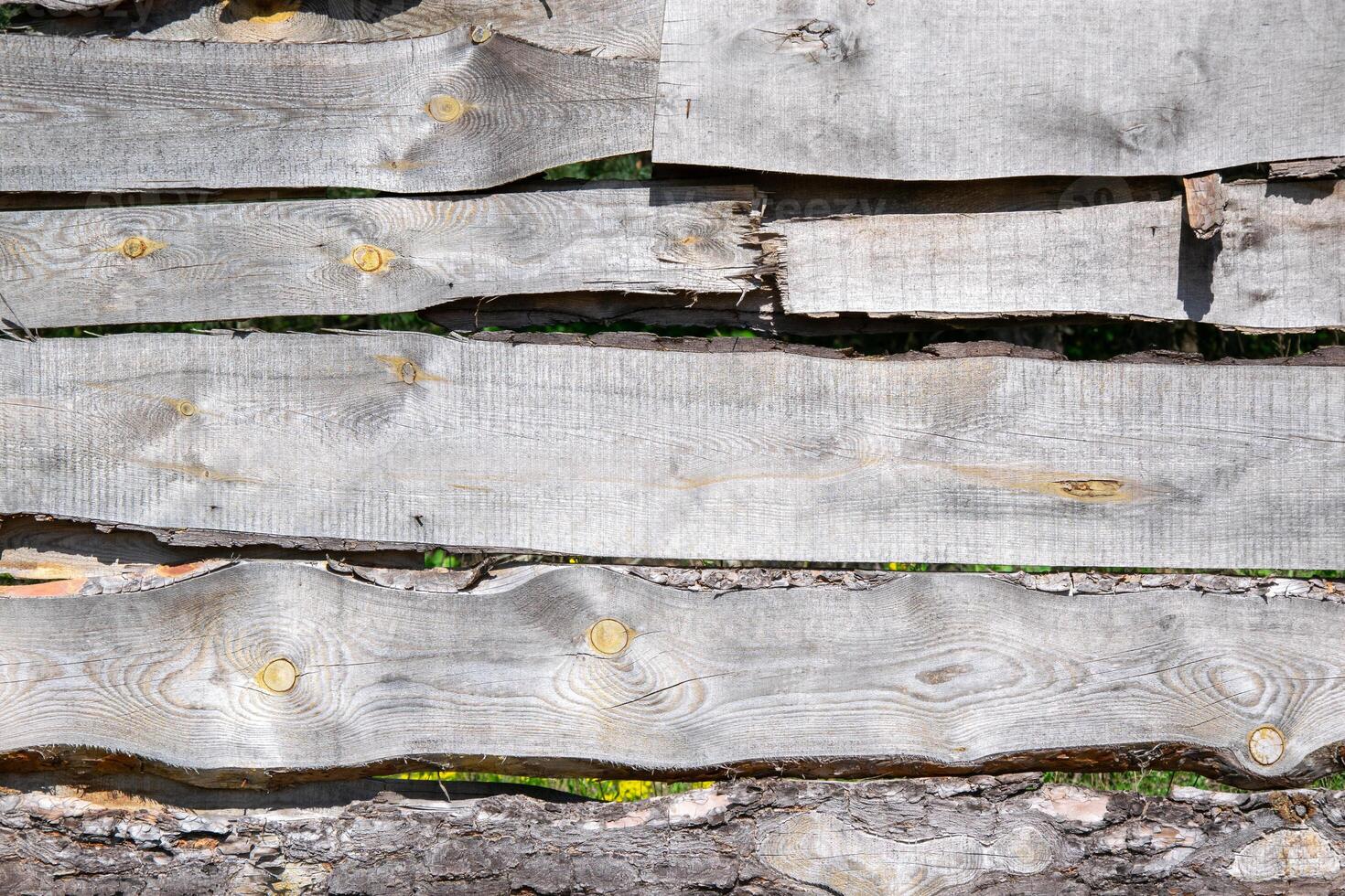 Close-up of weathered wooden fence panels with knots and grain patterns. Panels arranged horizontally with grass peeking through. Wood looks gray and worn photo