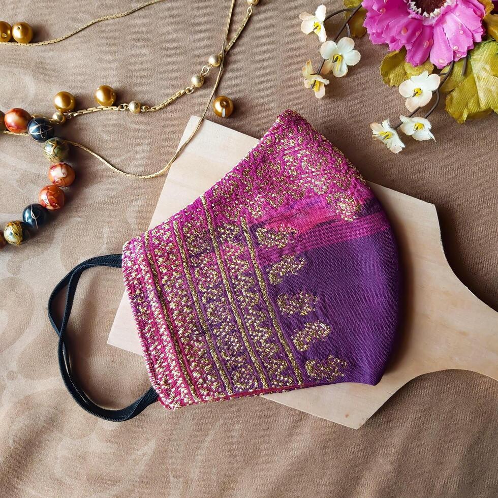 A handmade face mask made of traditional purple fabric with gold thread embellishments. photo