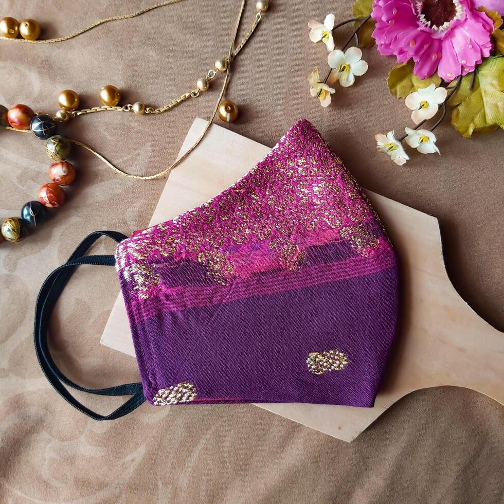 A handmade face mask made of traditional purple fabric with gold thread embellishments. photo