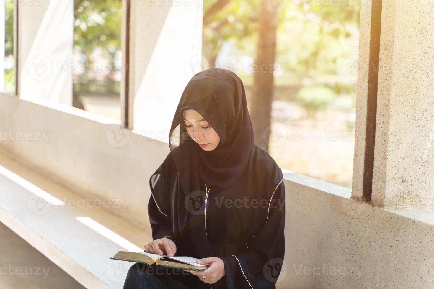 A beautiful Muslim students are intently reading Quran in the school building during breaks time in university with sun fare and blurred background. photo