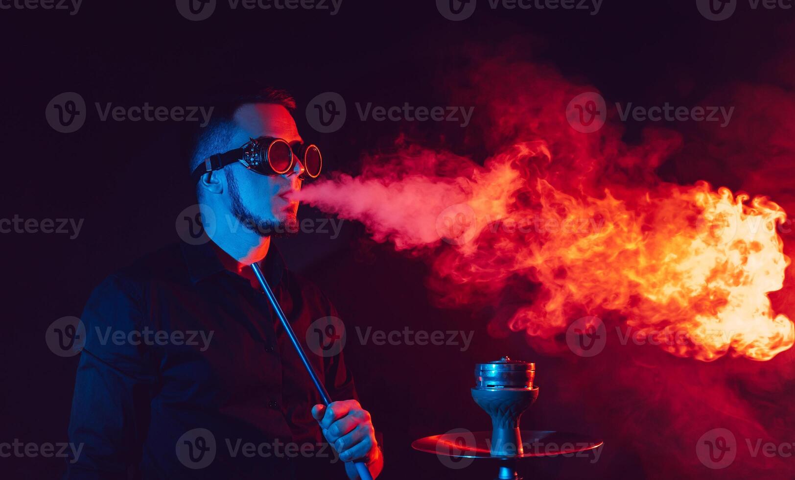 man in futuristic glasses smokes a hookah and blows a cloud of smoke in a shisha bar photo