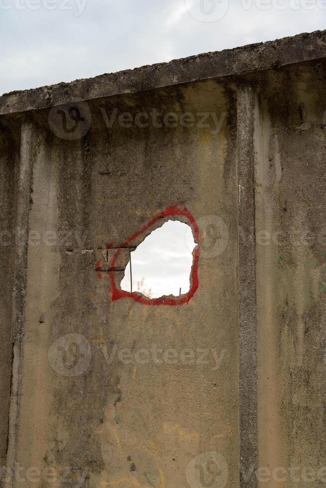 A hole in a concrete fence with a red circle drawn around it photo