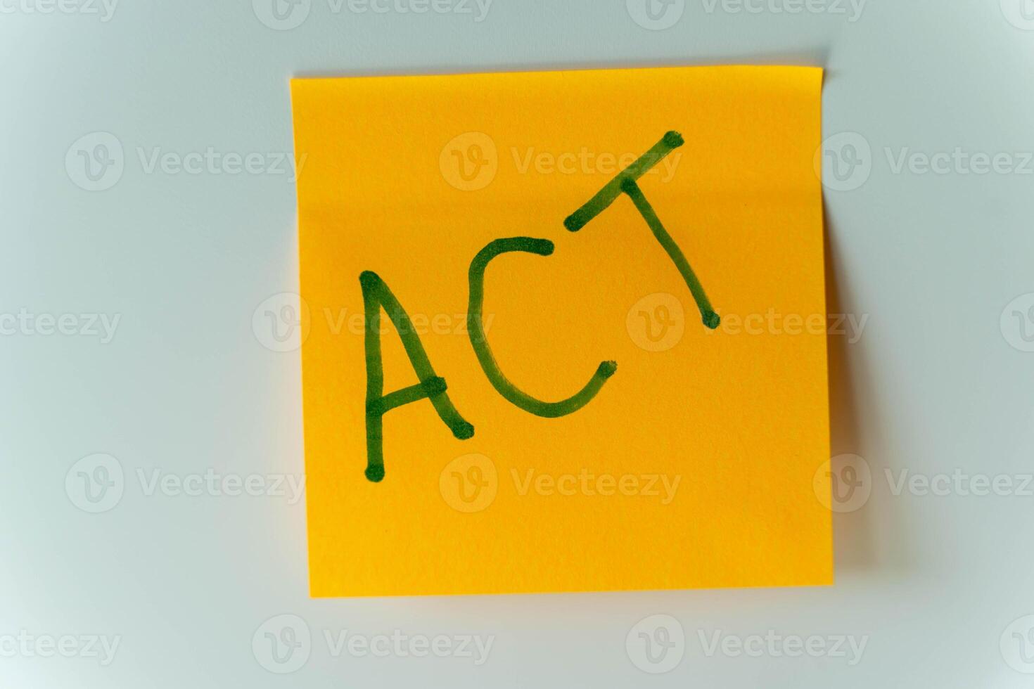 A yellow sticky note on a white fridge with the word ACT written on it in green photo