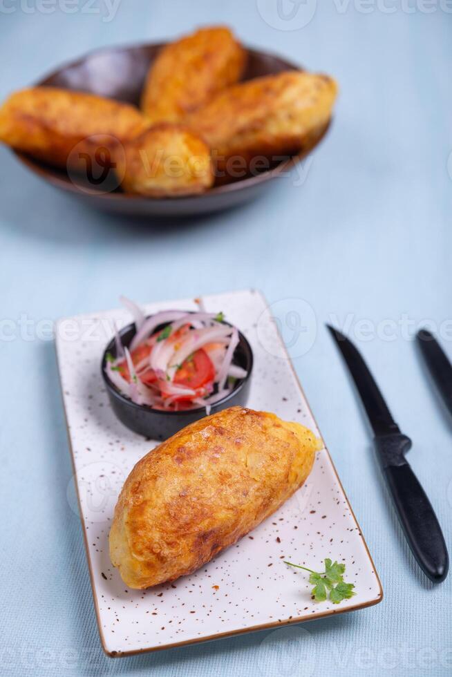 Top view of a crispy potato with a salty filling inside, accompanied by an onion and tomato salad. photo