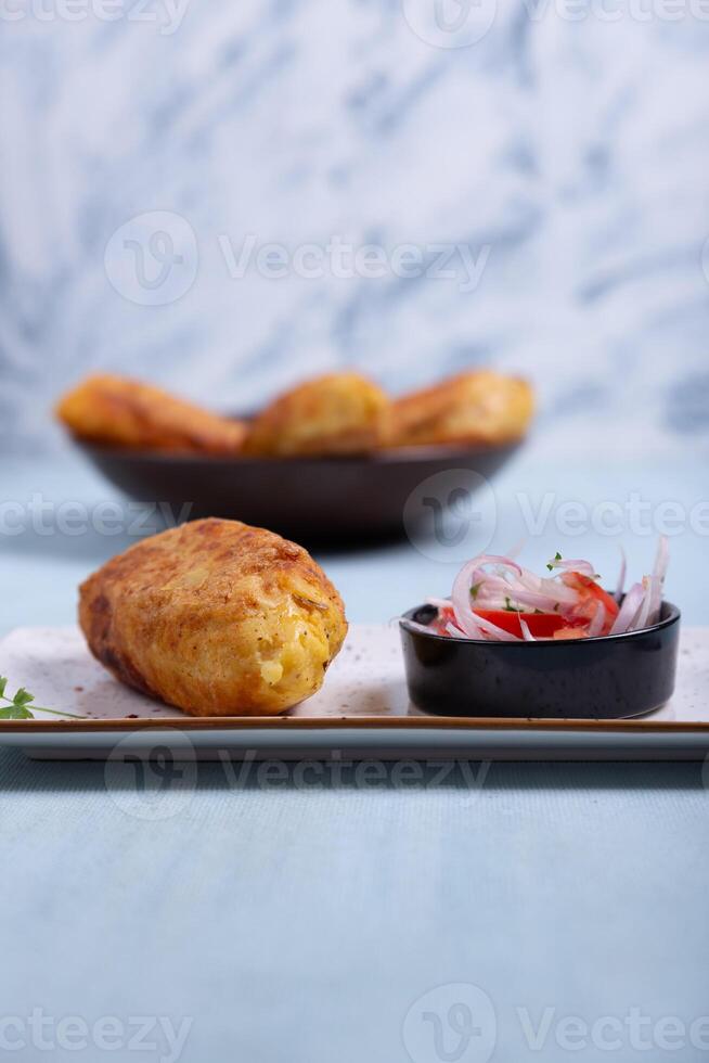 Front view of a crispy potato with a meat filling inside, accompanied by an onion and tomato salad. photo