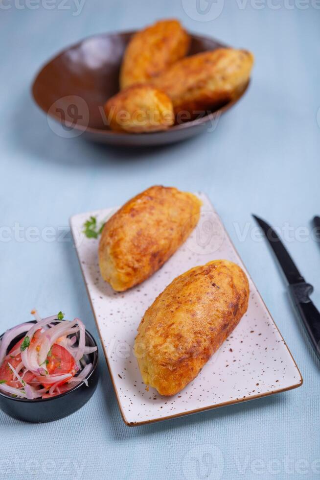 Appetizing Peruvian starter crispy stuffed potatoes on a plate, accompanied by an onion and tomato salad. photo
